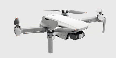 Grå DJI Mini 4K drone med fjernkontrol og tilbehør fra Fly More Combo vist på hvid baggrund.