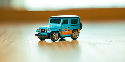 Mini Land Cruiser i blå/orange på bord set skråt forfra på et bord med sløret baggrund