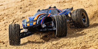 Grøn Traxxas Rustler 4x4 VXL fjernstyret bil i fuld fart på støvet grusvej med opspvirvlende jord.