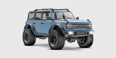 Mørkeblå Traxxas TRX-4M Ford Bronco crawler i skala 1:18 kører gennem mudret terræn i naturen.