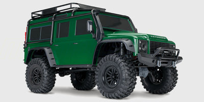 Grøn Traxxas TRX-4 Land Rover Defender crawler der kører gennem mudret terræn i naturen.