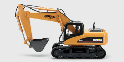 Gul fjernstyret gravemaskine med metalskovl og fjernbetjening vist på en hvid baggrund.