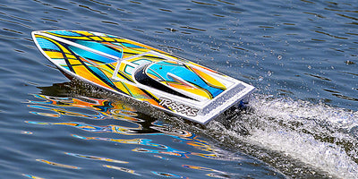 Hvid Traxxas Blast fjernstyret båd med røde og blå detaljer i fuld fart på vandet.